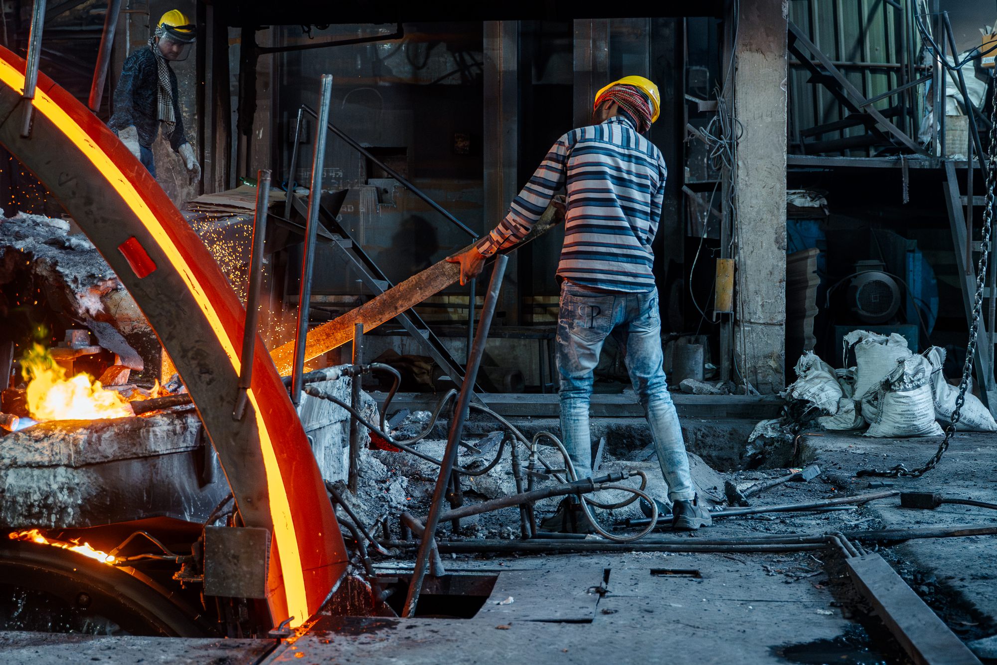 A worker at the furnace as a red-hot copper bar emerges
