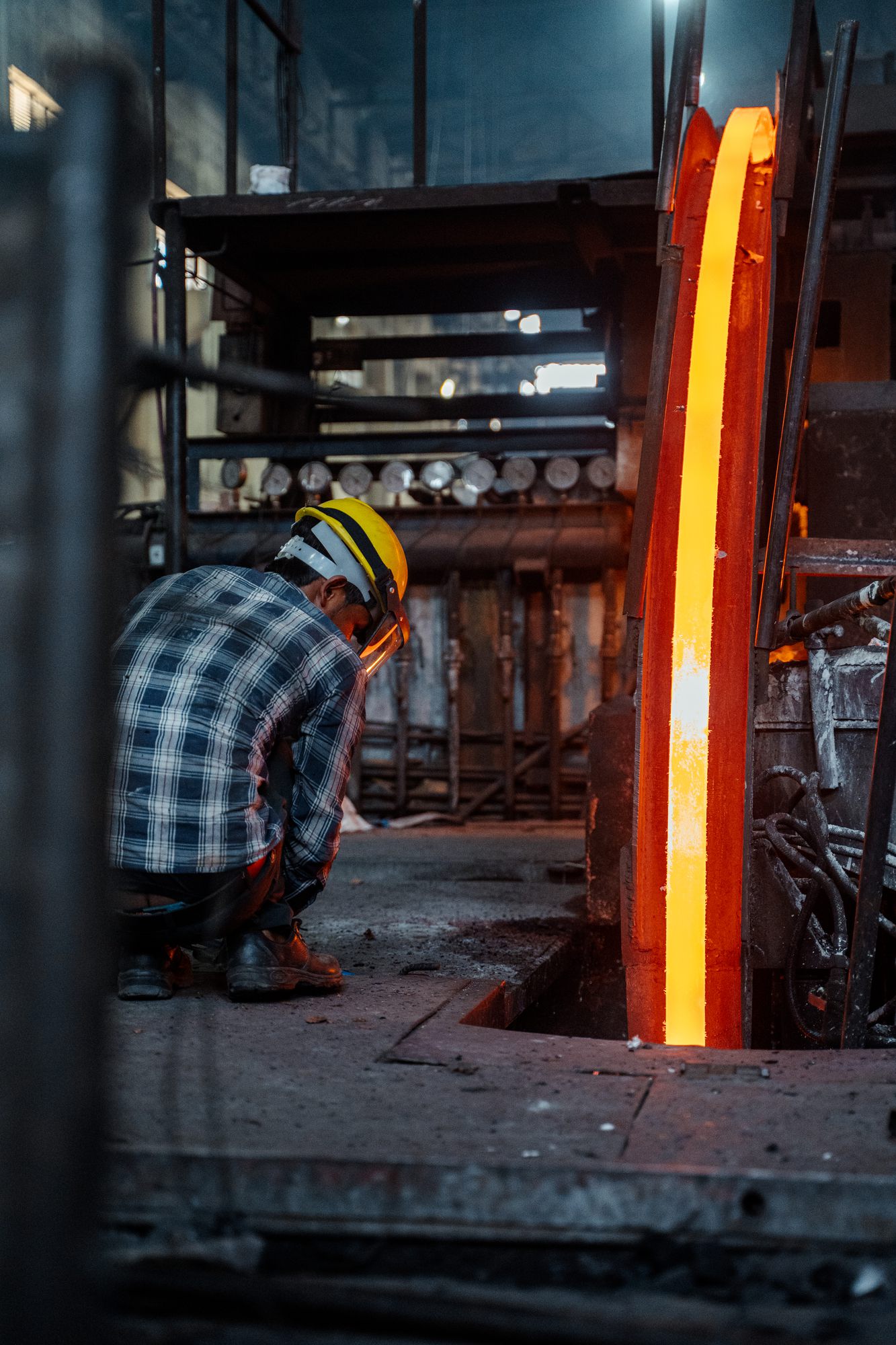 A worker crouched beside a red-hot copper bar in the mill